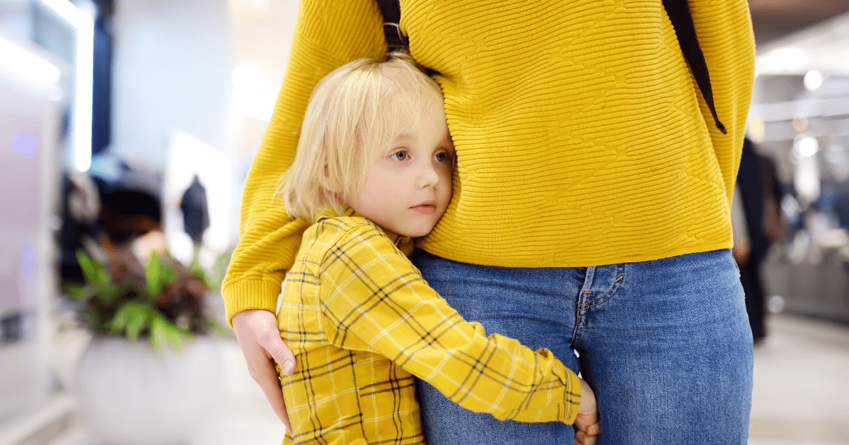 Young child clinging to mothers leg.