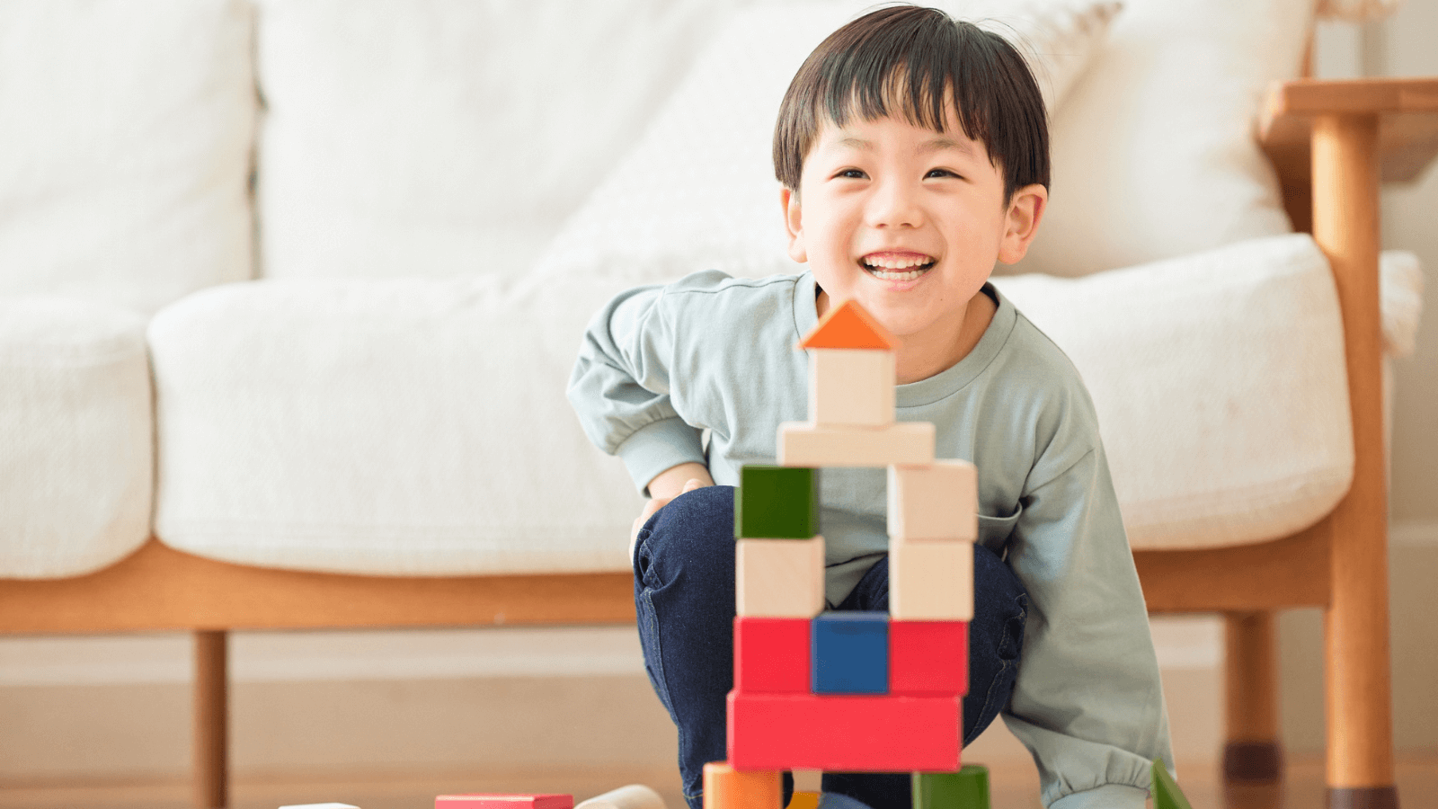 Smiling young boy sitting on the floor with a colorful tower of blocks in front of him.