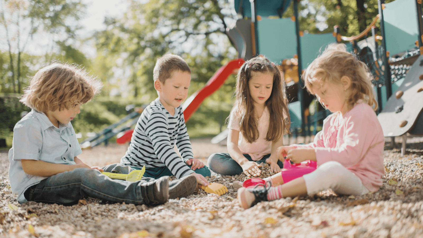 Four young children playing together on a playground, sharing toys and interacting in a group.