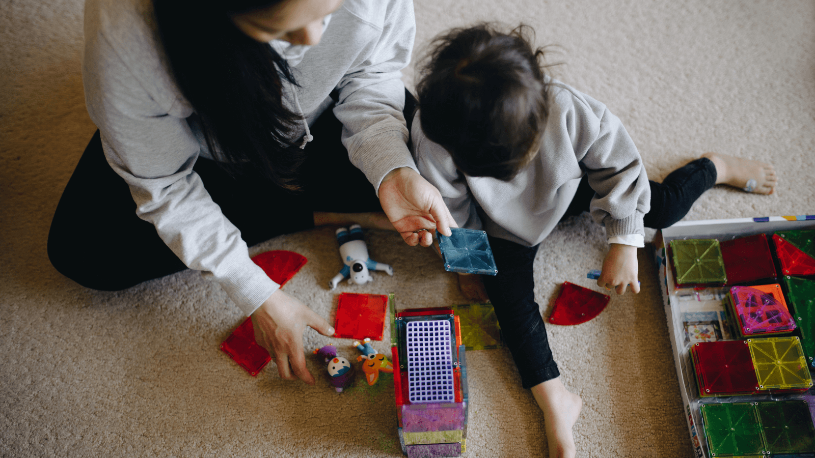 Nanny and child building colorful block structures on the floor during playtime.