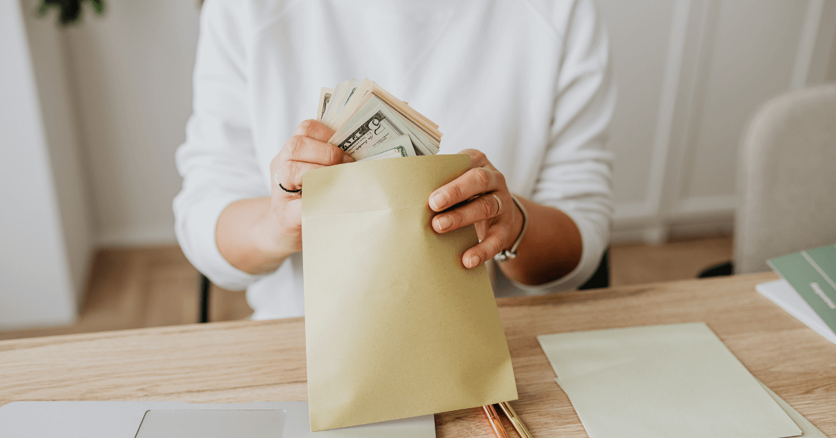 Person putting stacks of cash into a large envelope at a desk.
