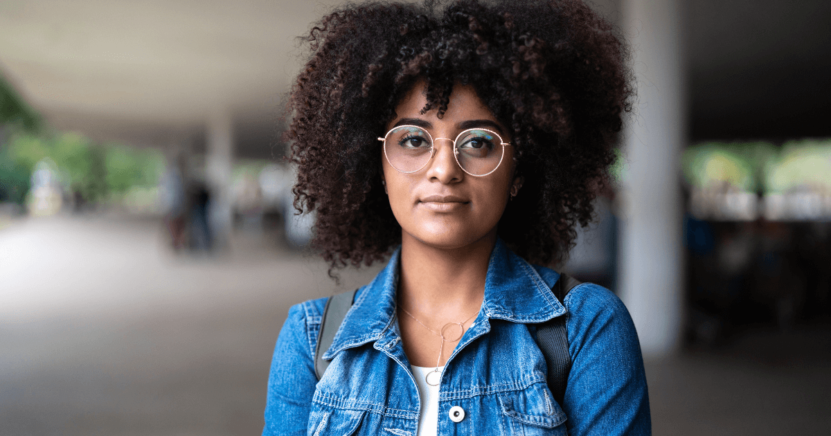 Confident woman with curly hair wearing glasses, looking directly at the camera.