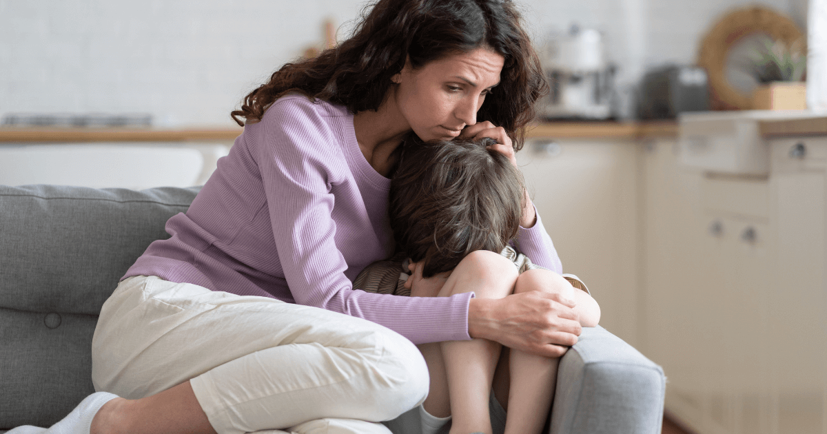 Mother comforting a sad child while sitting on a couch in the kitchen